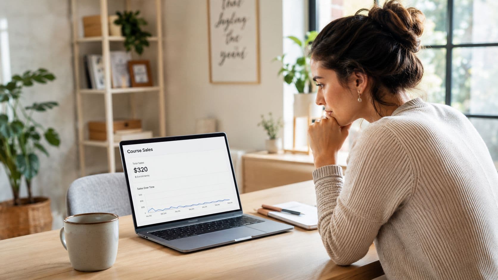 A woman reviewing her online course sales analytics on a laptop screen while sitting at her desk.