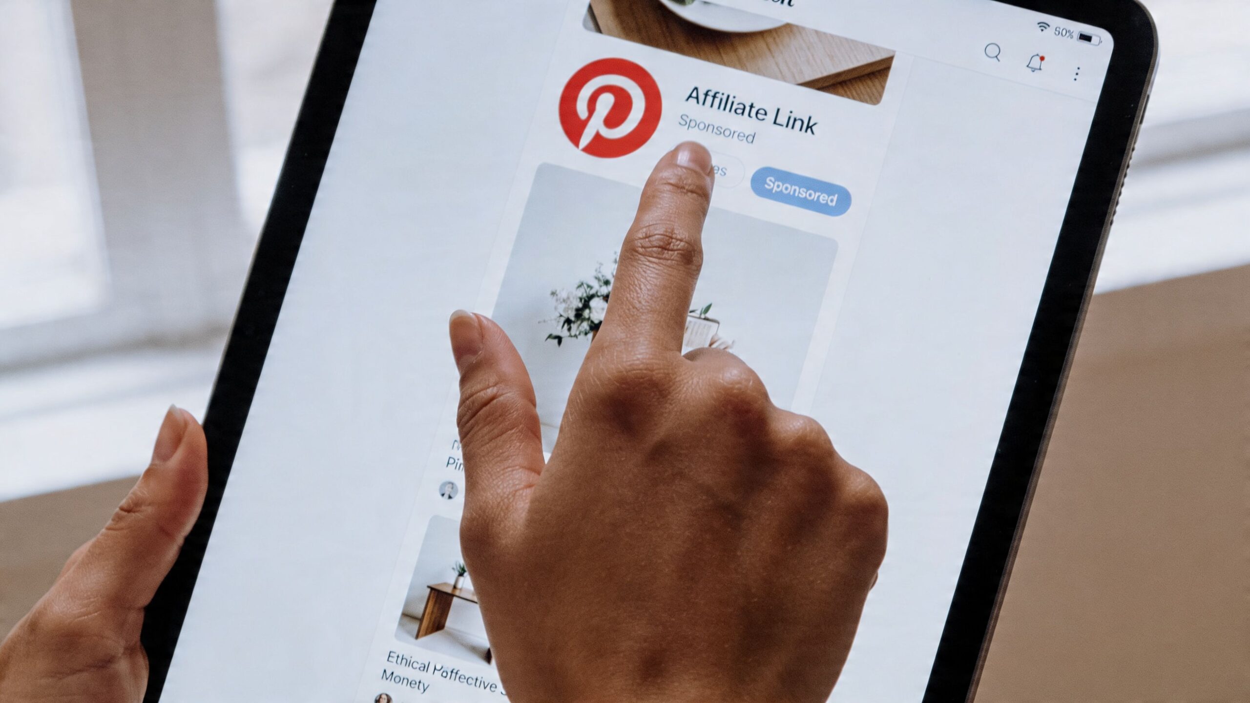 A close-up view of a person using a finger to tap an affiliate link ad on Pinterest.